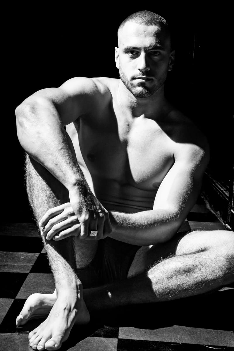 Jeremy Pouch accroupi sur un sol en damier, en noir et blanc