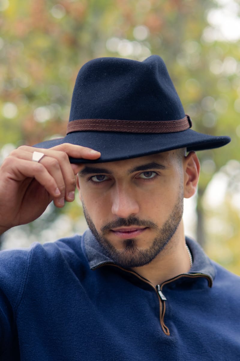 Portrait de Jeremy Pouch, chapeau feutre et pull bleu, en extérieur à l'automne