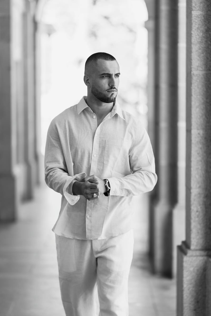 Jeremy Pouch en chemise blanche, debout sous une colonnade, en noir et blanc