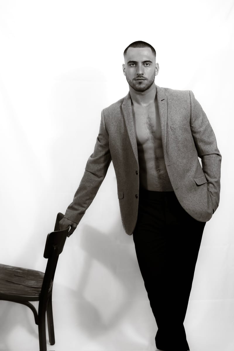 Jeremy Pouch en costume clair, assis sur une chaise en studio